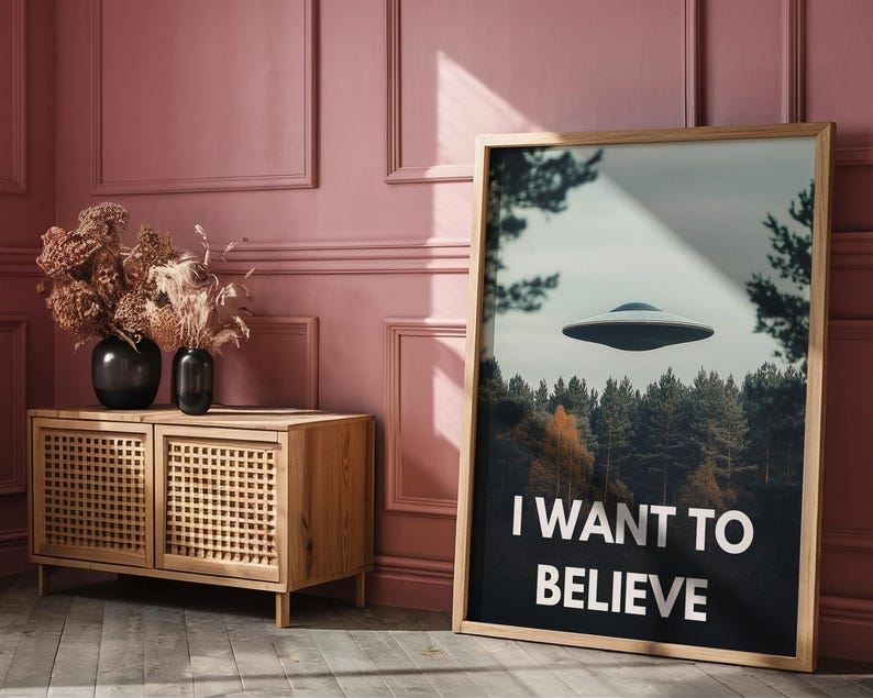 May include: A framed poster with a black and white image of a flying saucer over a forest. The poster has the text "I WANT TO BELIEVE" in white letters.