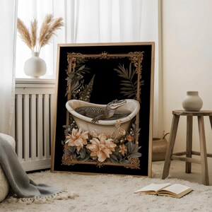 May include: Art print depicting an alligator in a bathtub, set against a black backdrop with a gold frame. The artwork incorporates floral and botanical details in soft colours. The framed print is displayed in a room with natural light and a neutral colour palette.