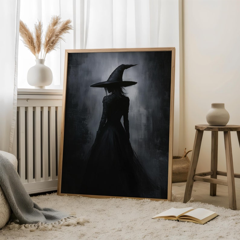 May include: A framed painting of a woman in a black dress and a pointed witch hat, standing in a dark, misty forest. The painting is in a wooden frame and is hanging on a white wall.