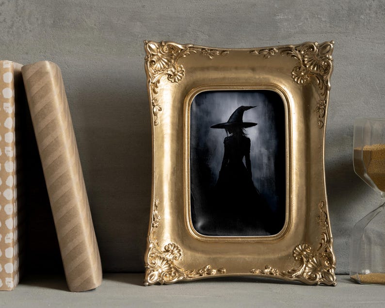 May include: A framed black and white illustration of a witch wearing a pointed hat and a long dress. The frame is gold and ornate.