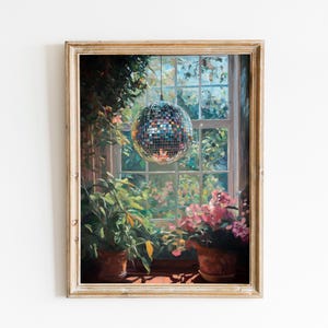May include: A framed painting of a disco ball suspended in front of a window overlooking a garden. The scene includes green foliage, pink flowers, and two potted plants on a windowsill. The frame is a light, warm colour.