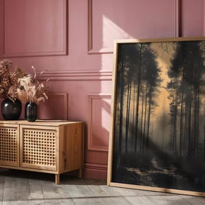 May include: A wooden cabinet with two doors and a woven rattan design. The cabinet is in front of a pink wall with white trim. A large framed print of a forest scene hangs on the wall.