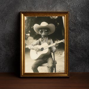 May include: A black and white photo in a gold frame of an alien wearing a cowboy hat and playing a guitar.