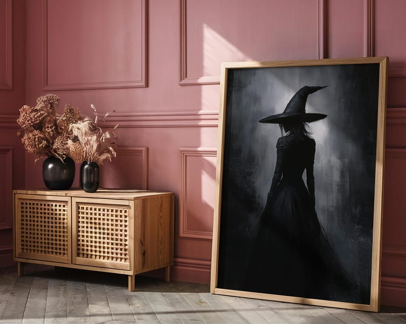 May include: A framed black and white illustration of a woman wearing a witch's hat and dress, standing in a foggy forest. The frame is made of wood and has a light brown finish.