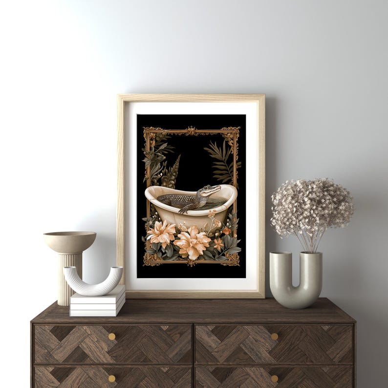 May include: Framed art print depicting an alligator in a bathtub, set against a black backdrop with gold and cream floral and botanical details. The frame is a light wood colour.