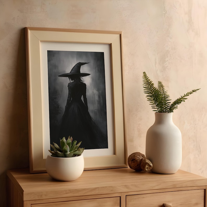 May include: A framed black and white illustration of a woman wearing a witch's hat and dress. The woman is standing in a dark forest setting. The frame is light wood and has a white mat.