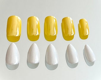 May include: A set of press-on nails in two styles and colors. Five yellow, rectangular nails are arranged above five white, almond-shaped nails. The nails are glossy and reflect light, suggesting a gel or acrylic finish. The background is a plain white surface.