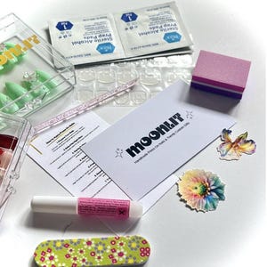 May include: A nail kit with various components, including press-on nails, alcohol prep pads, nail glue, a nail file, and a nail buffer. The kit also includes a card with the text "moonlit" and instructions.