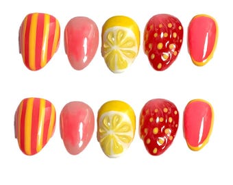 May include: A set of ten press-on nails with a fruit theme. Designs include yellow and orange striped nails, solid pink nails, lemon slice nails, strawberry nails, and pink nails with yellow borders. The nails are oval-shaped and glossy.