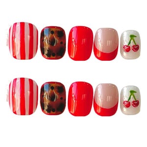 May include: A set of ten artificial nails in various designs. The designs include red and white stripes, tortoiseshell, solid red, a red French tip, and a clear nail with a cherry design. The nails are square-shaped.
