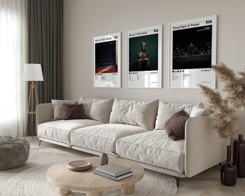 Op de afbeelding: Drie ingelijste muziek-albumhoezen aan een witte muur in een woonkamer. De albumhoezen zijn voor de albums "This Is What I Mean" van Stormzy, "Heavy Is The Head" van Stormzy en "Gang Signs & Prayer" van Stormzy. De albumhoezen zijn allemaal zwart-wit en tonen Stormzy op de voorkant.