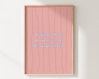 May include: A framed art print with a pink background and vertical wavy lines. The text "I kinda like it when you call me wonderful" is written in blue, handwritten-style font. The frame is a light wood color.
