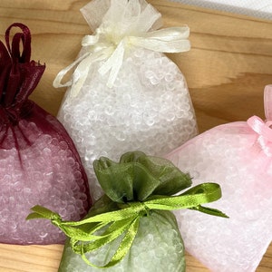 Pode incluir: Quatro pequenas bolsas de cordão cheias de contas de gel transparentes. As bolsas são feitas de tecido transparente nas cores bordô, branco, rosa e verde.