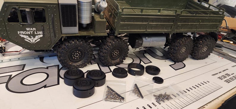 Pu&ograve; includere: Un camion giocattolo verde con la scritta "WAR FRONT LINI" in bianco sul lato. Il camion ha ruote nere ed &egrave; circondato da pezzi di plastica nera e piccoli sacchetti di viti.