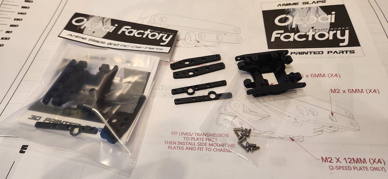 K&ouml;nnte beinhalten: Nahaufnahme eines Sets aus schwarzen Kunststoffteilen f&uuml;r ein 3D-gedrucktes RC-Auto. Die Teile sind mit "Oppai Factory" beschriftet und beinhalten Montageanweisungen. Die Teile umfassen ein Getriebe, seitliche Montageplatten und Schrauben.