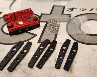 May include: A collection of mechanical parts, including a red metal component, six black elongated pieces with holes, and a small bag of silver screws. The parts are arranged on a patterned surface.