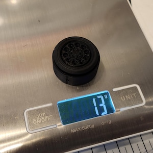 Pu&ograve; includere: Una ruota di plastica nera con un design dettagliato pesa 13 grammi su una bilancia digitale.