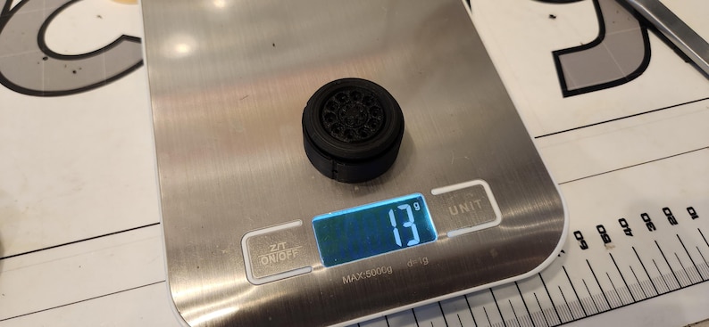 Pu&ograve; includere: Una ruota di plastica nera con un design dettagliato pesa 13 grammi su una bilancia digitale.