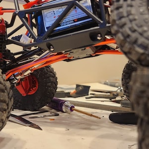 K&ouml;nnte beinhalten: Ein schwarzer und orangefarbener ferngesteuerter Rock-Crawler mit gro&szlig;en schwarzen Reifen. Das Auto ist angehoben und die Reifen sind &uuml;bereinander gestapelt. Das Auto hat ein schwarzes Chassis und einen roten Sto&szlig;d&auml;mpfer.