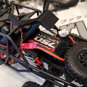 Puede incluir: Un coche de control remoto negro y rojo con una jaula de seguridad negra y una bater&iacute;a roja. La bater&iacute;a est&aacute; etiquetada como "25C Lipo 7.4V".