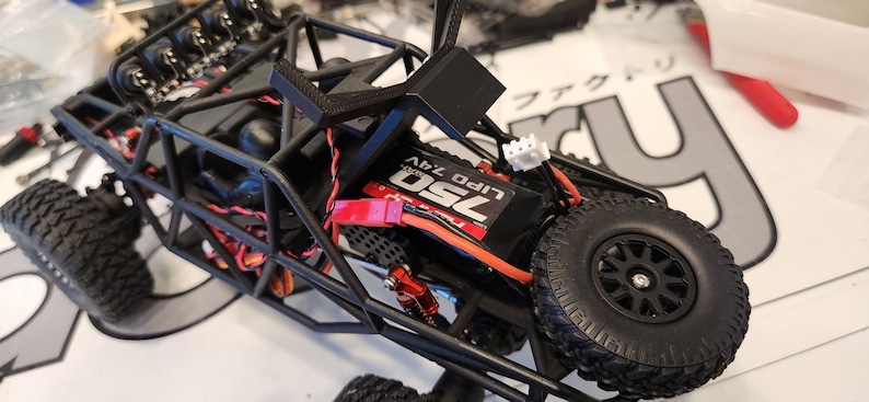 Puede incluir: Un coche de control remoto negro y rojo con una jaula de seguridad negra y una bater&iacute;a roja. La bater&iacute;a est&aacute; etiquetada como "25C Lipo 7.4V".