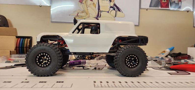 Puede incluir: Coche RC blanco con ruedas negras y una jaula antivuelco negra. El coche tiene una carrocer&iacute;a blanca y un interior negro. El coche est&aacute; sentado sobre una superficie blanca.