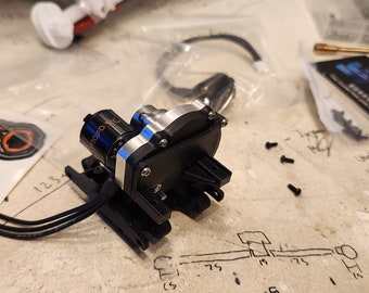 May include: A close-up of a small, black and silver electric motor with wires attached. The motor is on a white surface with a few screws and a small screwdriver nearby.