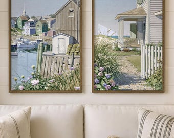 May include: A set of two framed wall art prints depicting coastal scenes. The left print shows a harbor with boats, wooden buildings, and flowers. The right print features a house with a porch, a white picket fence, and garden greenery.