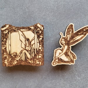 May include: Two wooden fairy ornaments, one with a fairy in a frame and the other with a fairy with wings spread out.