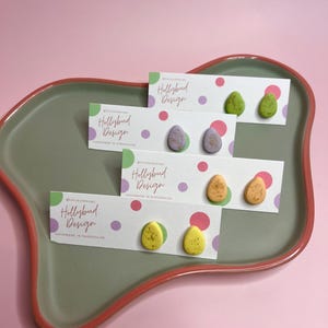 May include: Four pairs of handmade polymer clay earrings in various colours, including green, yellow, and purple. Each pair is displayed on a white card with the text "Hollybud Design" and "Handmade in Shropshire".
