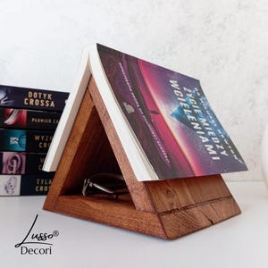 Peut inclure: Un support à livre en bois triangulaire avec un livre intitulé "La Vie Entre Les Vies" de Michael Newton posé dessus. Le support a une petite étagère pour les lunettes ou autres petits objets.