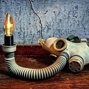 Peut inclure: Une lampe unique fabriquée à partir d'un masque à gaz vintage et d'une ampoule décorative. La lampe comprend un masque de couleur crème, un tube flexible et nervuré et une base noire. L'ampoule émet une lueur chaleureuse, créant une esthétique industrielle et artistique.