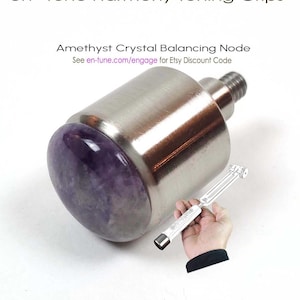 May include: Amethyst crystal balancing node, a silver-toned metal tuning fork with a purple amethyst crystal at the end. The text "en-tune" is visible on the tuning fork. The text "Amethyst Crystal Balancing Node" and "See en-tune.com/engage for Etsy Discount Code" is visible above the tuning fork.