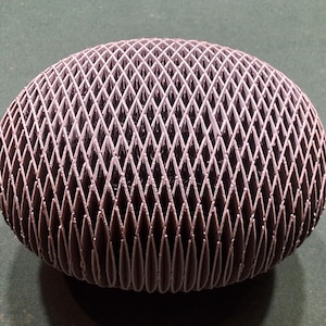 May include: A dark gray, spherical object with a lattice-like design. The intricate pattern creates a textured surface, with a series of diamond-shaped openings. The object appears to be made of a rigid material, possibly plastic or metal.