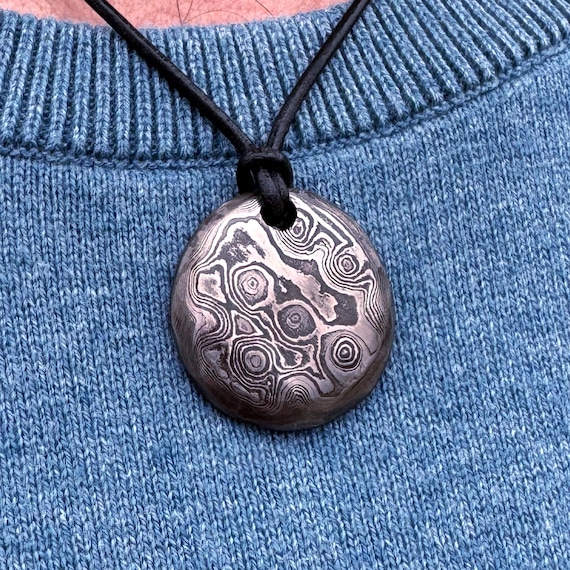 Round Damascus steel pendant with the swirling layered-metal pattern fully visible — a steel anniversary gift that actually looks like the material it celebrates.