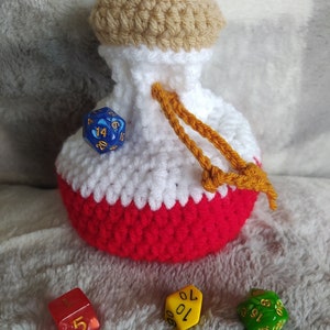 May include: Crocheted dice bag with a white and red body, a tan top, and a yellow drawstring. Four dice are visible: a blue d20, a red d6, a yellow d10, and a green d8.