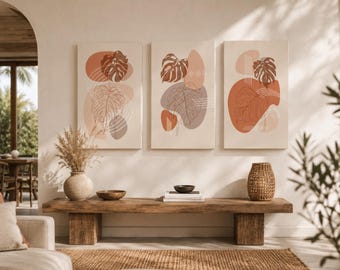 May include: A set of three rectangular wall art canvases featuring abstract botanical line drawings of monstera leaves layered over organic shapes in shades of terracotta, beige, and muted brown, displayed in a row on a light-colored wall.