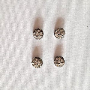 以下が含まれることがあります： クリアなラインストーンがついた銀色の丸いボタンが4つ。ボタンは2列に2つずつ並んでいます。