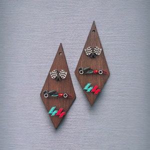 May include: Wooden diamond-shaped earrings featuring racing-themed designs. Each earring has a checkered flag, a race car, and the number "44" in teal and red. The earrings are dark brown with a small hole at the top.