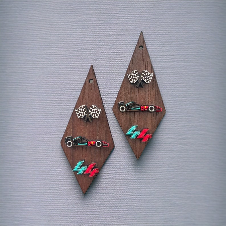 May include: Wooden diamond-shaped earrings featuring racing-themed designs. Each earring has a checkered flag, a race car, and the number "44" in teal and red. The earrings are dark brown with a small hole at the top.