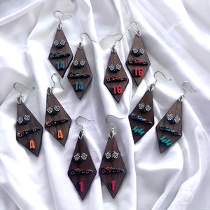 May include: Wooden diamond-shaped earrings with silver hooks. Each earring features a small race car, checkered flag, and a number. Numbers include 1, 4, 14, and 16. The earrings are on a white background.