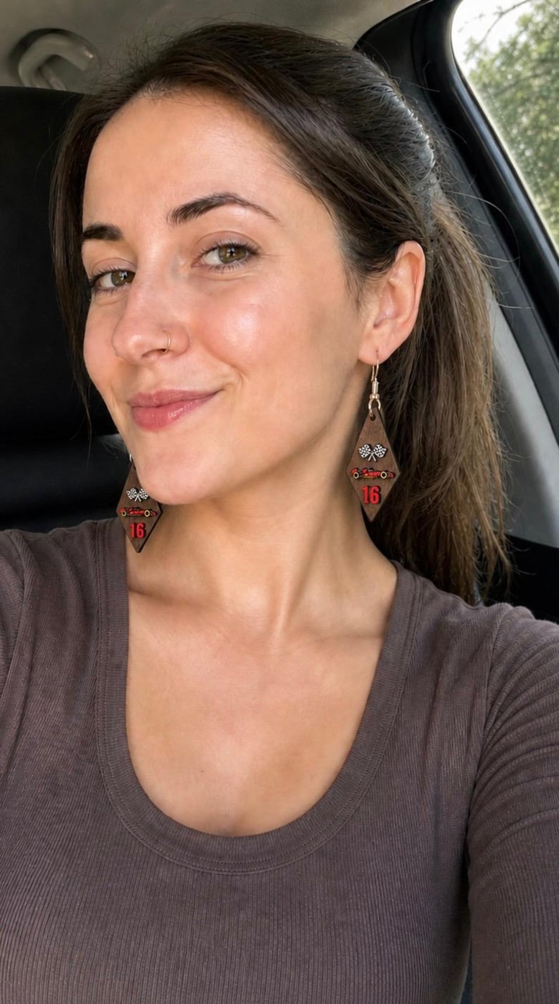 May include: Wooden diamond-shaped earrings with a racing theme. The earrings are brown with red and white accents, featuring a checkered flag design and the number 16. The earrings are hanging from gold-colored hooks.