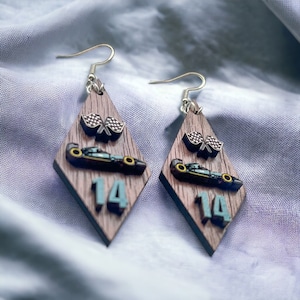 May include: A pair of diamond-shaped earrings with a wood grain pattern. Each earring features a race car, checkered flags, and the number 14 in teal. The earrings have silver-colored fish hook closures.