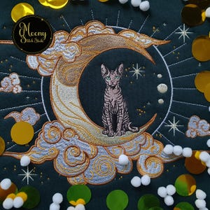 May include: An embroidered design of a cat on a crescent moon, with clouds and stars. The design uses gold, grey, and brown on a dark green background. The design includes the text "Moony Stitch Studio".