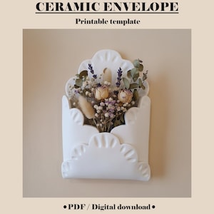 Può includere: Vaso da parete in ceramica bianca a forma di busta, riempito di fiori secchi. Il vaso ha un bordo smerlato ed è montato su una parete beige. Il testo in alto recita "CERAMIC ENVELOPE" e "Printable template".