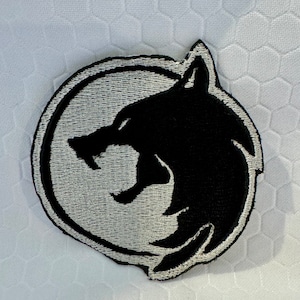 May include: A black and white embroidered patch featuring a wolf's head inside a circle.