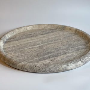 May include: A round, gray marble tray with a raised edge. The tray has a natural, veined pattern.
