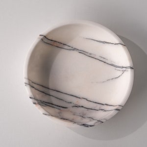 May include: A white marble bowl with black and pink veining. The bowl is round and has a smooth surface.
