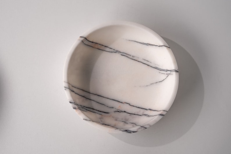 May include: A white marble bowl with black and pink veining. The bowl is round and has a smooth surface.