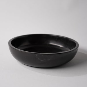 May include: A black, round, shallow bowl made of marble. The bowl has a smooth, polished surface.